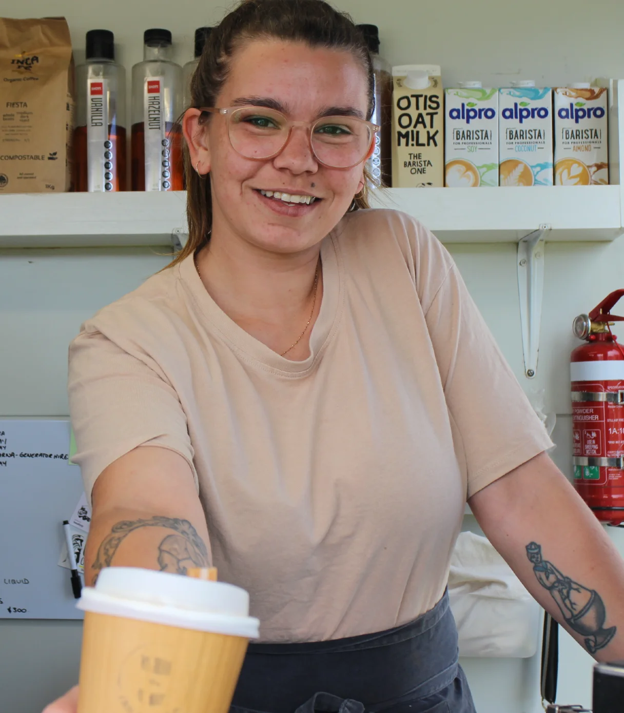 Fair Grinds Co. owner Kahli holding out a fresh cup of coffee.